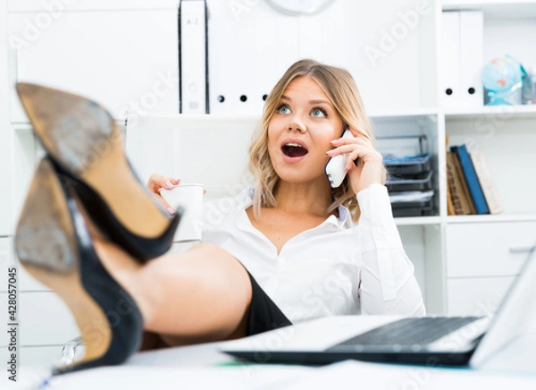 Fototapeta Relaxed girl threw her legs on table and spoke on phone at office. High quality photo