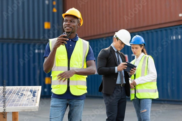 Obraz African factory worker or engineer using walkie talkie for preparing a job in containers warehouse storage