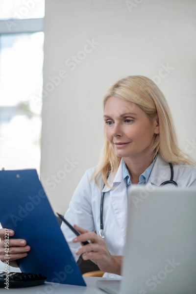 Fototapeta Concerned female doctor reading document in office