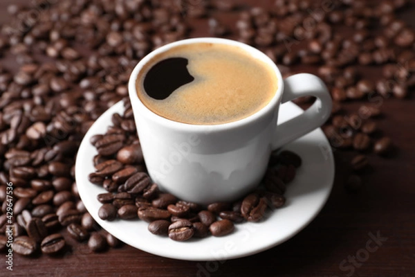 Fototapeta Cup of hot aromatic coffee and roasted beans on wooden table, closeup