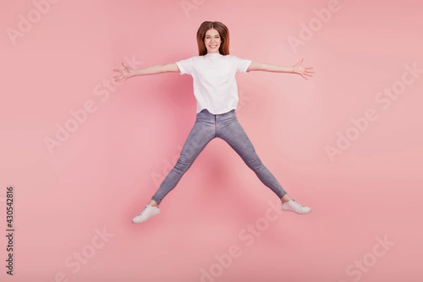 Fototapeta Photo of funky positive girl jump high up star shape on pink wall wear white t-shirt jeans sneakers