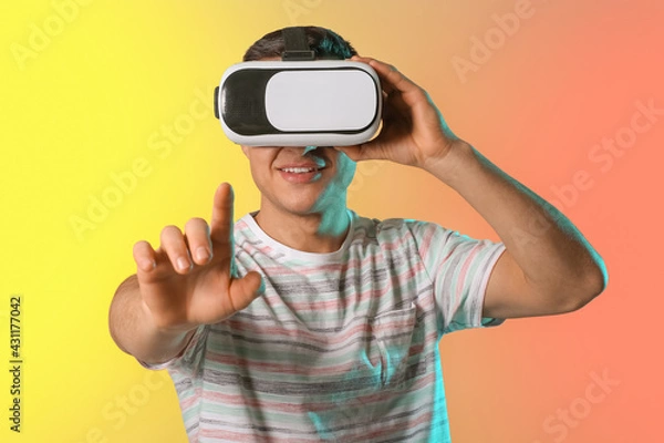 Fototapeta Young man with virtual reality glasses on color background