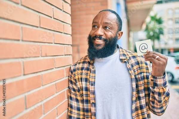 Fototapeta Handsome modern african american man with beard smiling positive standing at the street showing email symbol on paper