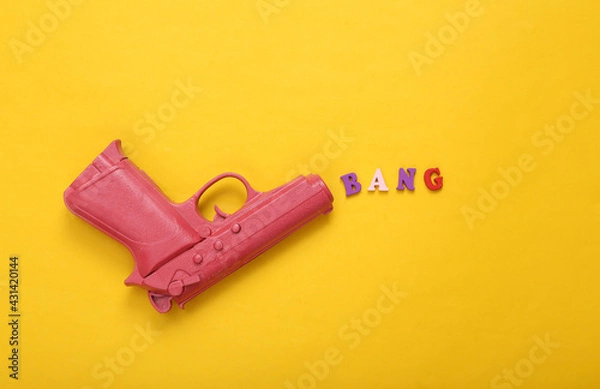 Fototapeta Pink pistol gun shooting word bang on yellow background. Creative minimalism layout. Flat lay. Top view