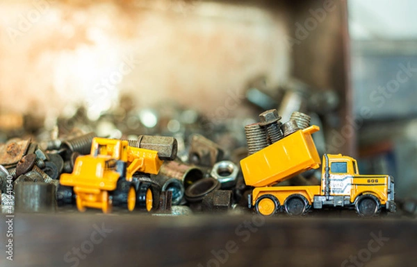 Fototapeta Yellow toy dump truck and typewriter tractor bulldozer with pile of old screws nuts and bolts