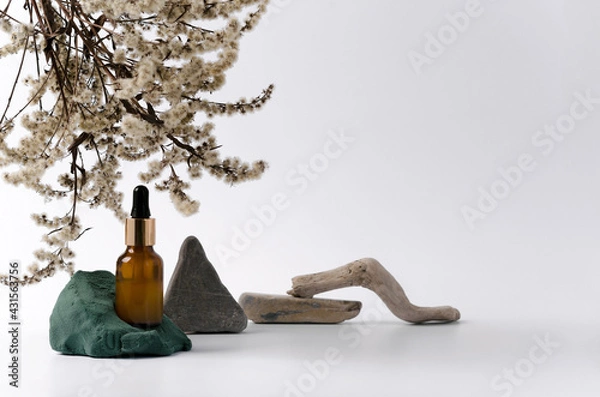 Fototapeta Serum in a bottle of dark glass with a pipette on the background with natural decorative elements stone, twigs, dry flowers on a white background. Concept layout showcasing goods with copying space