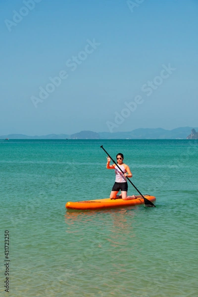 Fototapeta young sporty woman playing stand-up paddle board on the blue sea in sunny day of summer vacation