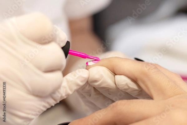 Fototapeta Manicure in a beauty salon. The manicure master covers the nails of a young girl with gel polish. Space for the text. The concept of professional care for hands and nails.