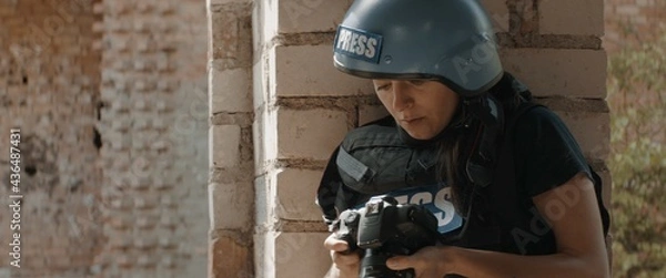 Obraz CU Portrait of Caucasian female war journalist wearing protective helmet and bulletproof vest gear taking photos under fire. Shot with 2x anamorphic lens