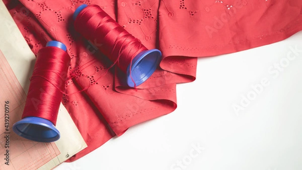 Fototapeta Tailoring accessories. Colorful thread spools with fabric on white table background. Red sewing string. Art, handicraft concept