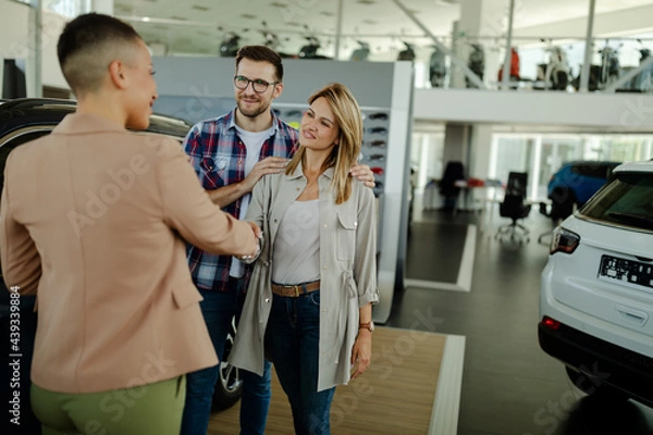 Fototapeta Saleswoman and customer shaking hands congratulating each other at the dealership showroom.