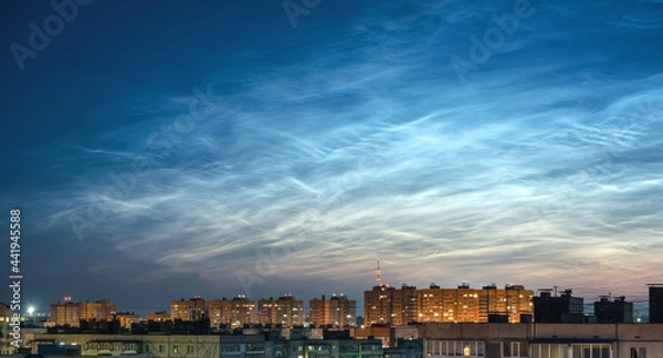 Fototapeta Wide panorama of the night sky and spectacular silvery clouds, silhouettes of city buildings against a background of shining clouds. Atmospheric phenomenon glowing of noctilucent clouds.