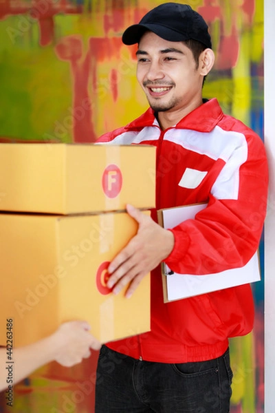 Fototapeta Smiling Asian courier man delivers packages to Asian female customer at home. Parcel delivery and shipping, door to door e-commerce business concept.