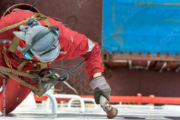 Fototapeta Seaman ship crew working aloft at height derusting and getting vessel ready for painting.