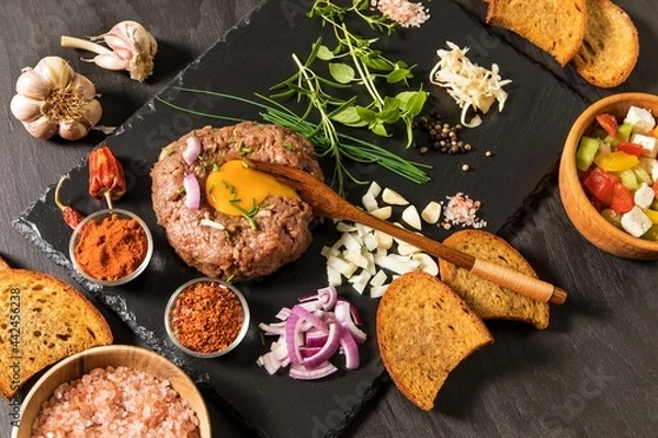 Fototapeta Steak tartar with chopped onion and herbs on a black slate board.Traditional homemade French steak tartare of raw beef.