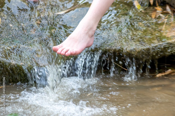 Fototapeta Young boy playing barefoot with clear water at a little creek using his feet and the water spring cooling his toes and legs and refreshing with the pure elixir of life in zen meditation atmosphere