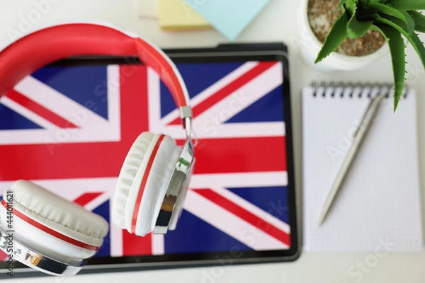 Fototapeta Tablet with image of British flag with headphones and notebook with pen lie on table