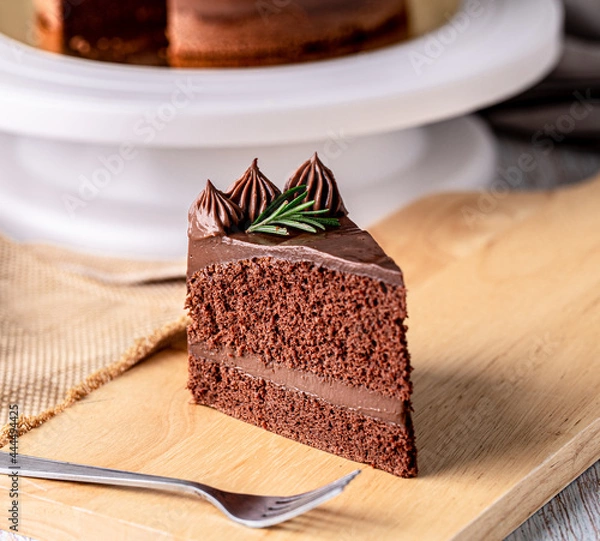 Obraz Slice of delicious homemade chocolate cake soft fudge paste on wooden board with fork for serve, closeup.