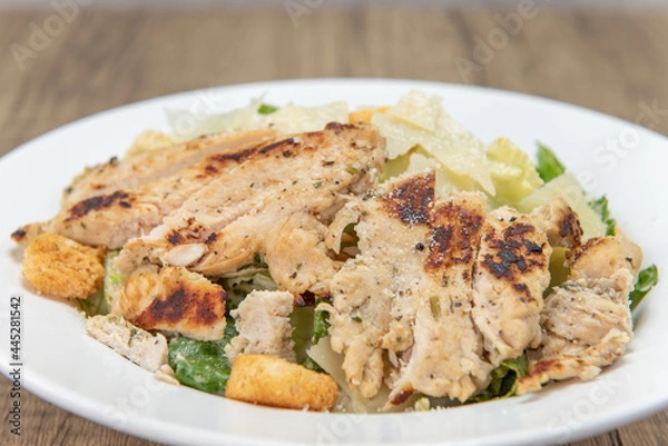 Fototapeta Large grilled chicken breast cut up and topping this very hearty caesar salad in a bowl