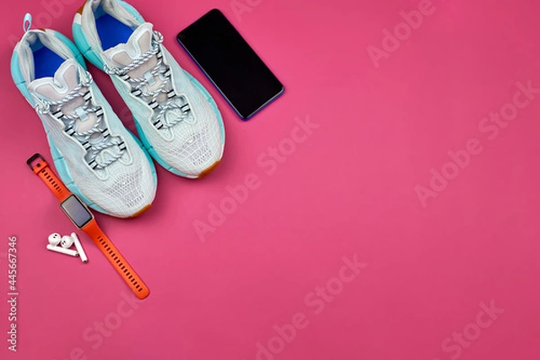 Fototapeta Modern gadgets for sports. Running shoes, a smartphone, a fitness watch and wireless headphones on a pink background. Sports equipment and clothing for training, top view