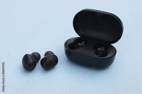 Fototapeta Wireless headphones or earbuds with charging case on bright blue background.