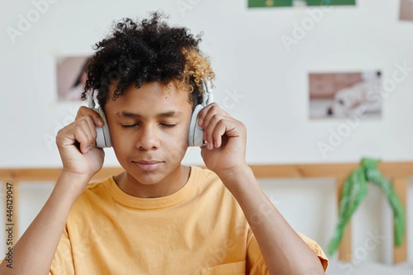 Fototapeta Portrait of mixed-race teenage boy wearing headphones and listening to music with eyes closed, copy space