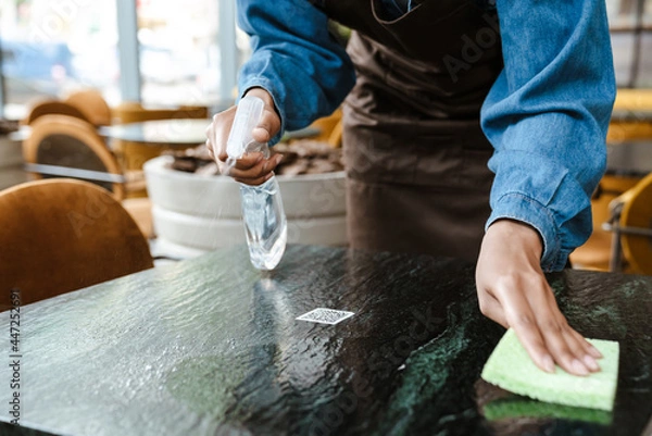 Obraz Black waitress wearing apron cleaning table while working in cafe