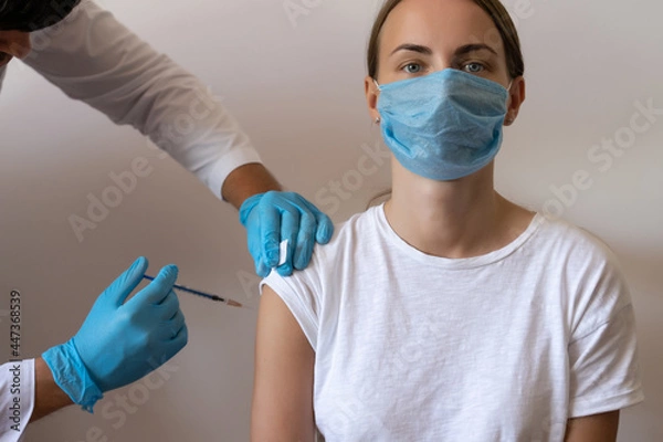 Obraz Woman and her doctor wearing face masks and getting a vaccine shot in a doctor's office. Doctor making injection to female patient in clinic