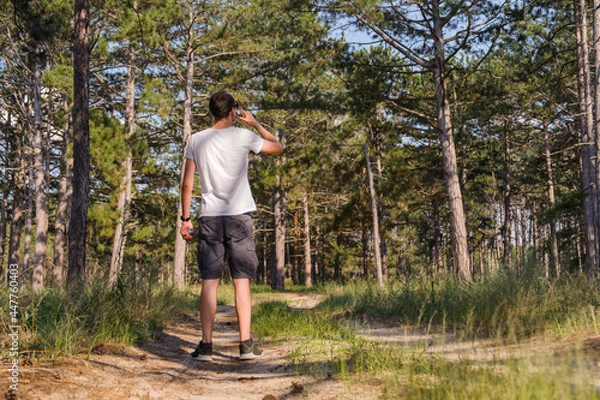 Fototapeta Man tourist on a forest path stopped to drink water