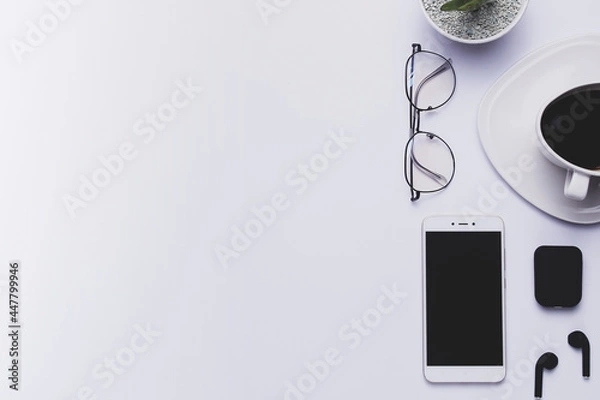 Fototapeta White office desk with, a cup of coffee, smartphone, potted plant, glasses,
earphones, and space for your creations. Top view.