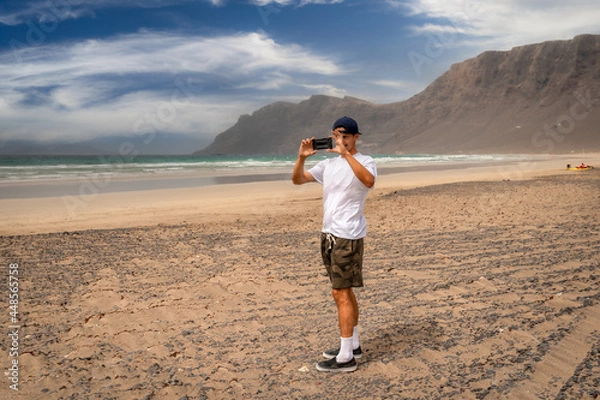 Fototapeta young man takes a picture on  Famara beach. Lanzarote. Canary Islands