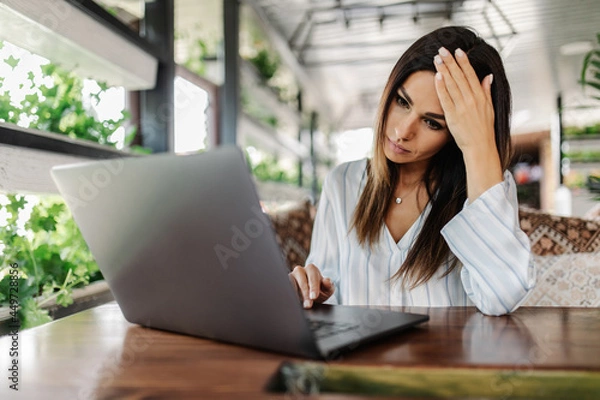 Obraz Young woman feeling depressed while using computer in cafeteria