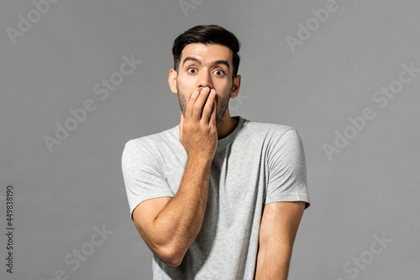 Fototapeta Portrait of shocked young Caucasian man with hand covering mouth on light gray studio background