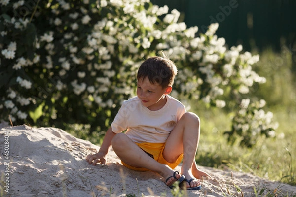 Fototapeta a boy in a beige T-shirt is sitting on the sand and playing with him