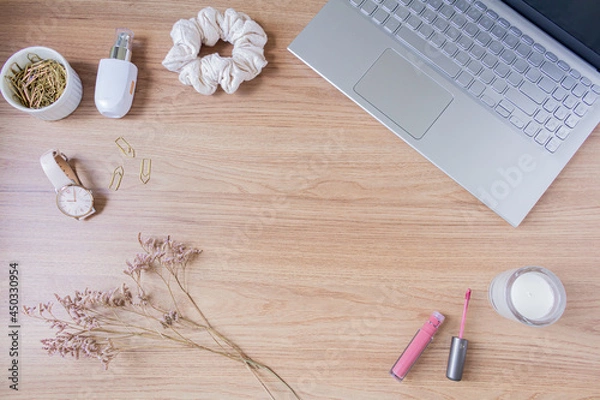 Fototapeta Beauty blog fashion concept. Female styled accessories: laptop, scrunchie, wildflowers and cosmetics on wooden background. Flat lay, top view trendy feminine background.