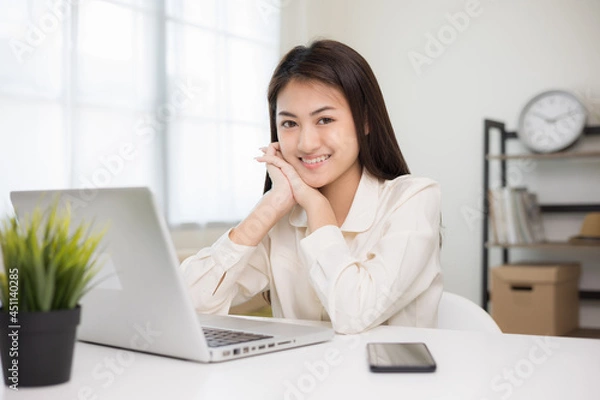 Fototapeta Young asian beautiful business woman working with laptop sitting at home. Smiling charming happy young female doing homework meeting conference with team at home.