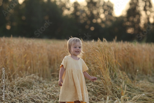 Fototapeta a little girl waves her arms, standing in the evening in the sunset sun