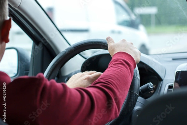 Fototapeta  Man in a red sweater is driving a car. Hands on the wheel