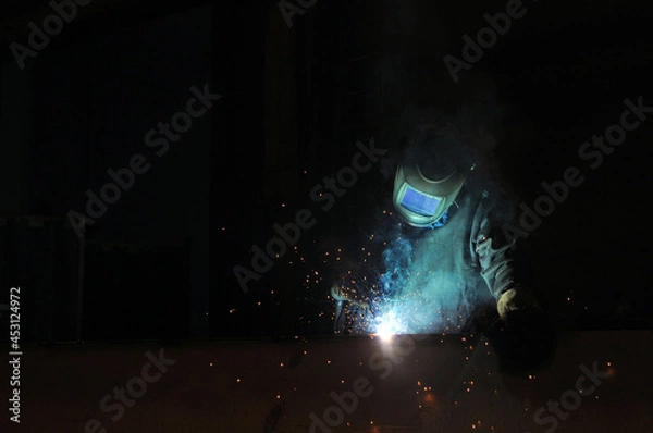 Fototapeta An electric welder welds metal structures at a factory.