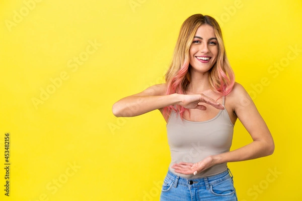 Fototapeta Young woman over isolated yellow background holding copyspace imaginary on the palm to insert an ad