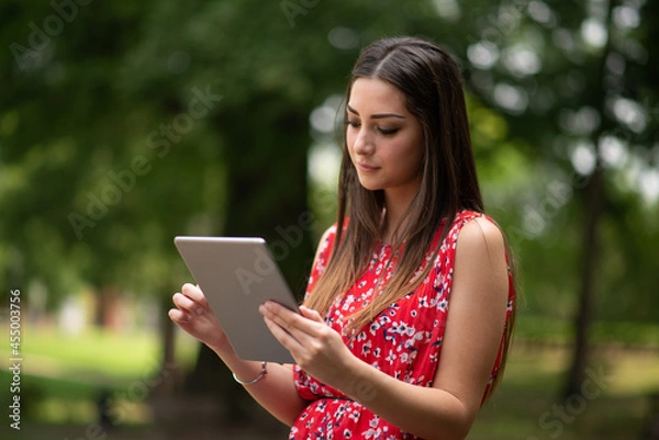 Fototapeta Woman using a digital tablet in the park