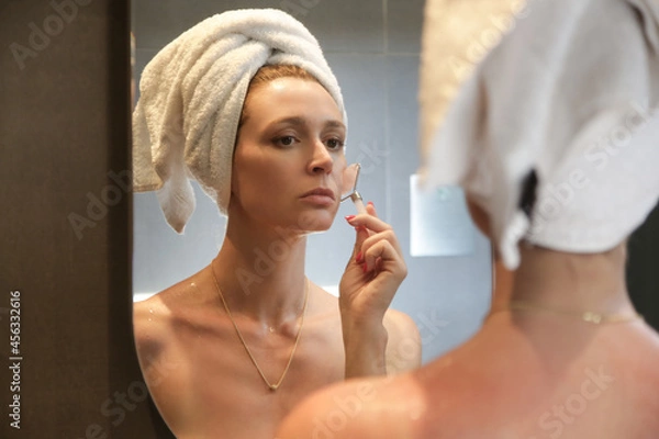 Fototapeta Face massage. Woman using rose quartz face roller for skin care.