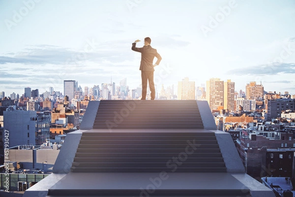 Fototapeta Back view of young caucasian male standing on top of stairs on bright city background with sky view. Leadership, growth and success concept.