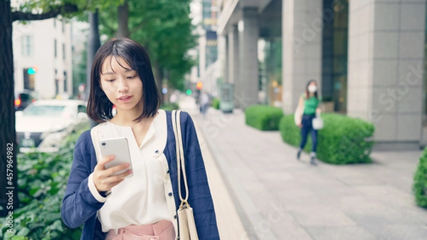 Fototapeta スマホを持って街を歩く女性