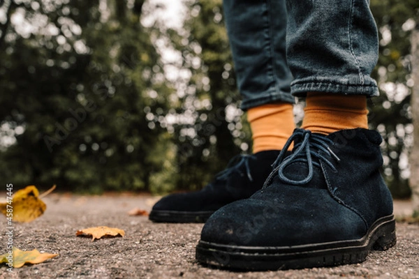 Fototapeta Close-up of legs in blue suede shoes and yellow socks. Asphalt with fallen leaves. Autumn fashion for men.