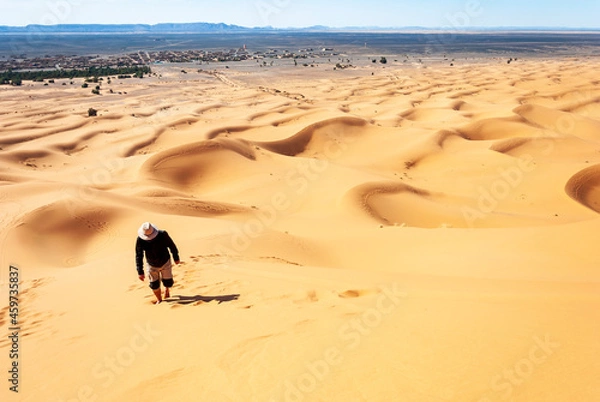 Fototapeta man walking with the desert dunes on his back