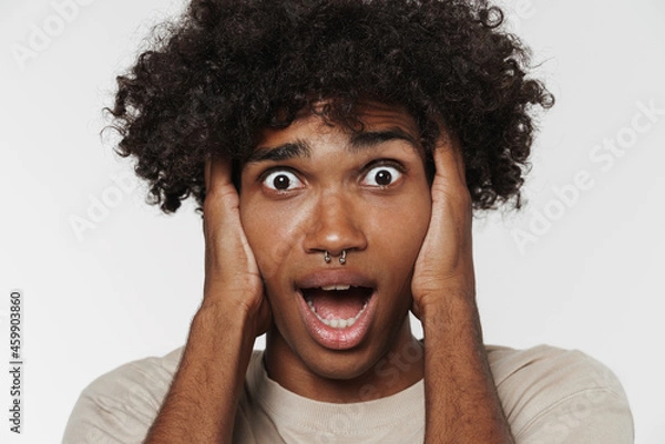 Fototapeta Young black man expressing surprise while holding his head