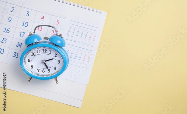 Obraz Alarm clock with calendar on yellow background.