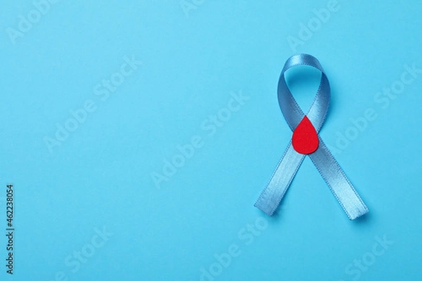 Fototapeta Light blue ribbon with paper blood drop on color background, top view and space for text. Diabetes awareness