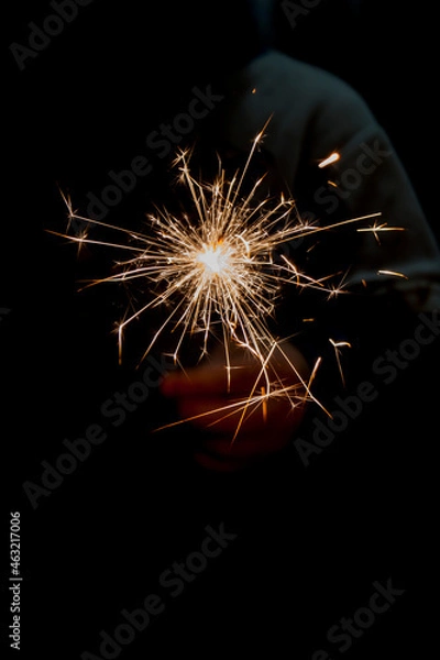 Fototapeta Burning Bengali fire on a dark background in a child's hand, make a wish for the new year, Christmas miracles and divination, baptism. Traditions